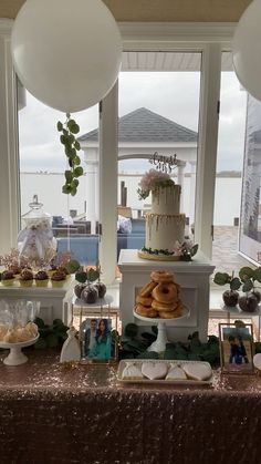 a table topped with cakes and desserts next to two large windows covered in balloons