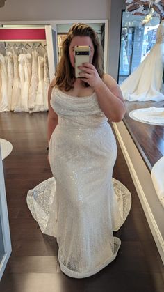 a woman in a white dress taking a selfie with her cell phone while wearing a wedding gown