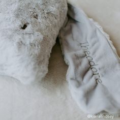 a white teddy bear laying on top of a bed next to a gray and white pillow