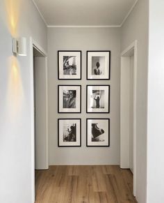 a hallway with white walls and pictures on the wall, along with wooden flooring