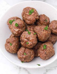 a white bowl filled with meatballs and garnished with parsley on top