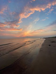 people are walking along the beach as the sun goes down in the distance with pink and blue clouds