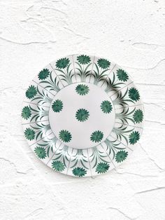 a green and white plate with leaves on the rim is hanging on a stucco wall