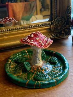 a small mushroom sitting on top of a green plate next to a gold framed mirror