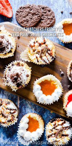 several cupcakes with white frosting and toppings on a wooden cutting board