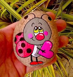 a hand holding a rock with a ladybug painted on it's face