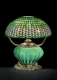 a green lamp sitting on top of a table next to a black background with an ornate glass shade