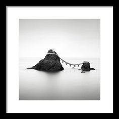 a black and white photo of rocks in the ocean with a rope hanging from them