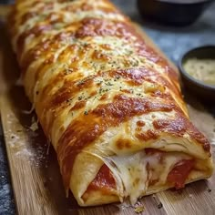 a large piece of pizza sitting on top of a cutting board next to some dipping sauces