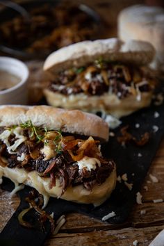 two sandwiches with meat, cheese and onions on a cutting board