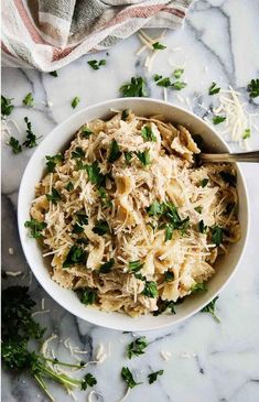 a white bowl filled with pasta and parsley on top of a marble countertop