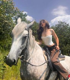 a woman riding on the back of a white horse in a field with tall grass