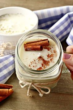 a person holding a spoon over a jar filled with cinnamons and yogurt