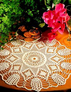 a crocheted doily sits on a table next to some flowers and cookies