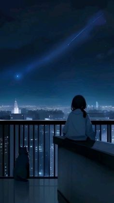 a person sitting on a balcony looking at the city lights in the distance with an airplane flying overhead