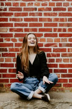 a woman sitting in front of a brick wall laughing