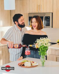 a man and woman are in the kitchen pouring something into a wine glass while standing next to each other