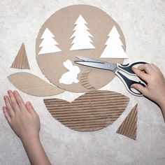 someone using scissors to cut out the paper shapes on top of cardboard circles with trees in the background