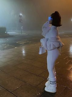 a woman in white is standing on the sidewalk at night with her cell phone up to her ear