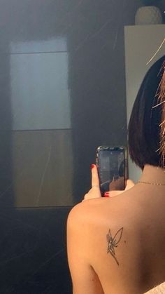 a woman taking a selfie in the mirror with her cell phone and tattoo on her back