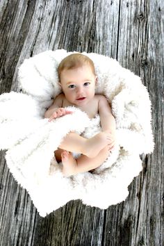 a baby wrapped in a white blanket laying on top of a wooden floor and looking up at the camera