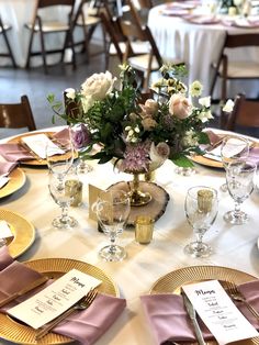 the table is set with gold plates and pink napkins, silverware, and floral centerpieces