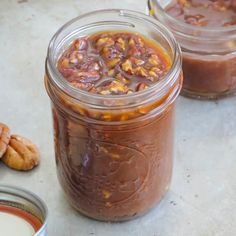 two jars filled with food sitting on top of a counter next to some pecans