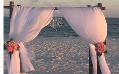 an outdoor wedding set up on the beach with flowers and draping over it