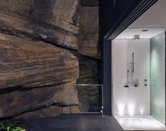 a bathroom with a walk in shower next to a large rock wall and glass door