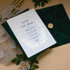 a green and white wedding card with a gold seal on it next to some flowers