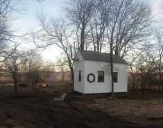 an old outhouse sits in the middle of a dirt field with bare trees around it