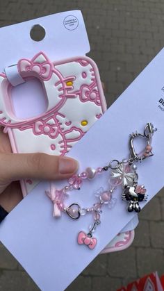 a person holding up a hello kitty phone case with charms on it's side