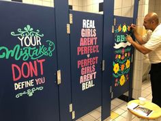 a man writing on the side of a blue locker in a public restroom that has been decorated with flowers and words