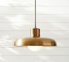 a gold colored light hanging from a ceiling fixture on a white wall with wood planks in the background