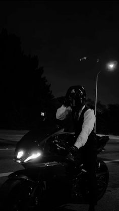 a man riding on the back of a black motorcycle at night with his helmet on