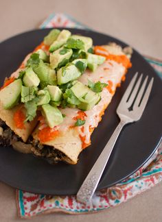 a black plate topped with an enchilada covered in cheese and avocado