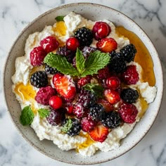 a bowl filled with fruit and cream on top of a marble countertop next to a spoon