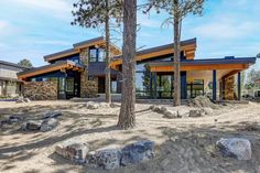 a large house surrounded by trees in the middle of a dirt field with rocks and boulders