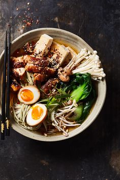 a bowl filled with noodles, meat and veggies next to chopsticks