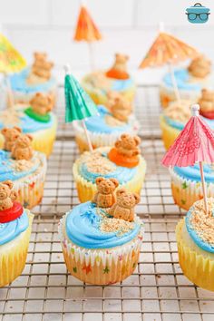 cupcakes decorated with teddy bears and umbrellas on a cooling rack for dessert