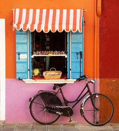 a bicycle parked in front of a window with blue shutters and a basket on it