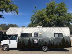 a camper van parked in front of a house with trees on the side and mountains behind it