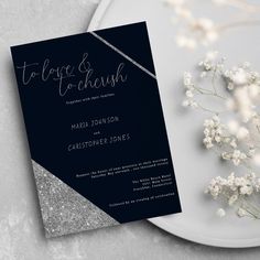 a black and silver wedding card on a plate next to some baby's breath flowers