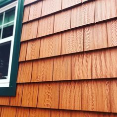 a dog is looking out the window of a wooden shingled house with green shutters