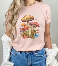 Introducing our latest creation - the Magic Mushroom T-Shirt, with a unique CottageCore twist! This botanical shirt is crafted from premium-quality cotton, ensuring a comfortable fit that is perfect for all-day wear. The vintage mushroom graphic is eye-catching and adds a touch of whimsy to any outfit. This botanical mushroom t-shirt is perfect for nature lovers, cottagecore enthusiasts, and anyone who appreciates a touch of magic in their wardrobe. The ribbed knit collars and dual side seams pr Mushroom Print Crew Neck Graphic T-shirt, Graphic Tee With Mushroom Design, Graphic Tee T-shirt With Mushroom Design, Spring Mushroom Print Graphic Tee, Spring Mushroom Print Short Sleeve T-shirt, Spring Mushroom Print Crew Neck T-shirt, Spring Mushroom Design Short Sleeve Tops, Spring Short Sleeve Top With Mushroom Design, Spring Crew Neck T-shirt With Mushroom Print