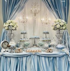 a table topped with lots of desserts under a chandelier covered in blue drapes