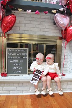 two babies are sitting on a mantle with red balloons and heart - shaped balloons in front of them