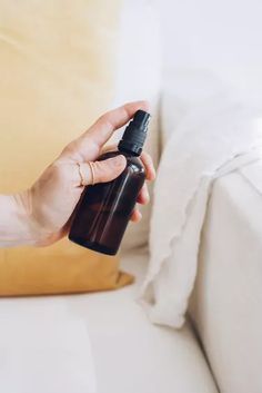 a person holding a spray bottle on top of a white couch next to a pillow