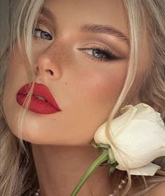 a woman with long blonde hair and red lipstick holding a white flower in her mouth