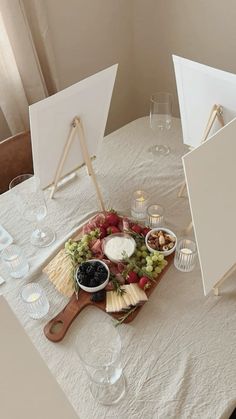 a table with two easels, cheese and fruit on it next to empty wine glasses